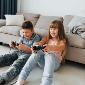 Chico y chica sentados en el suelo del salón, jugando a videojuegos.