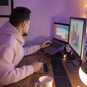 Hombre moreno con sudadera rosa trabajando un diseño con el ordenador